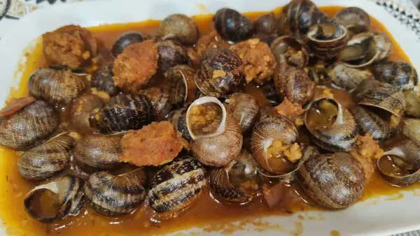 Un plato abundante de caracoles en salsa, con trozos de chorizo y especias, listo para disfrutar.