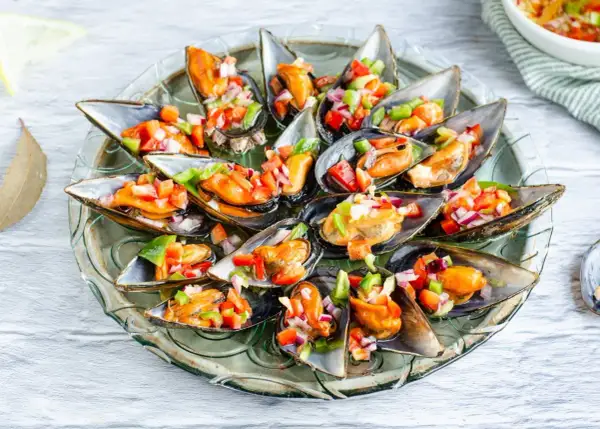 Mejillones a la vinagreta, frescos y coloridos, servidos en su concha con una picada de pimientos y cebolla.